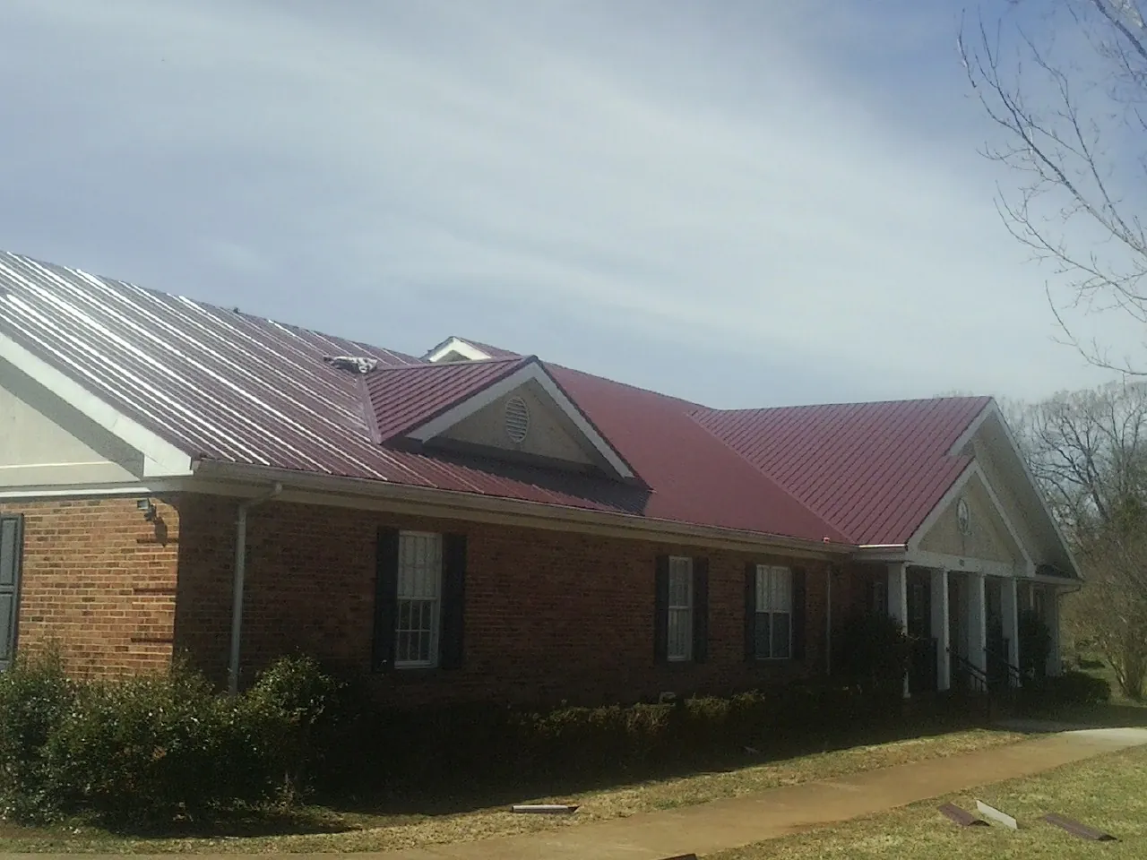 Red metal roof with gabled entries on a long brick building, from a Hail Damage Roof Repair job in Junction City